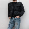A person wearing a black leather jacket and dark shirt with denim jeans displaying iron-on patches.