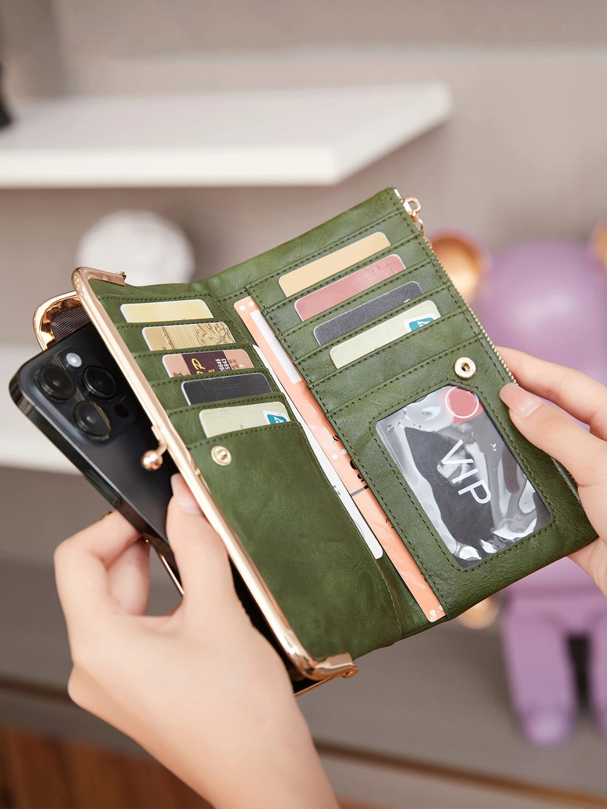 A hand holds a green leather wallet with multiple cards and a phone, resting on a light shelf.