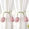 A set of pink tulip-shaped fabric tie backs used to secure white curtains.