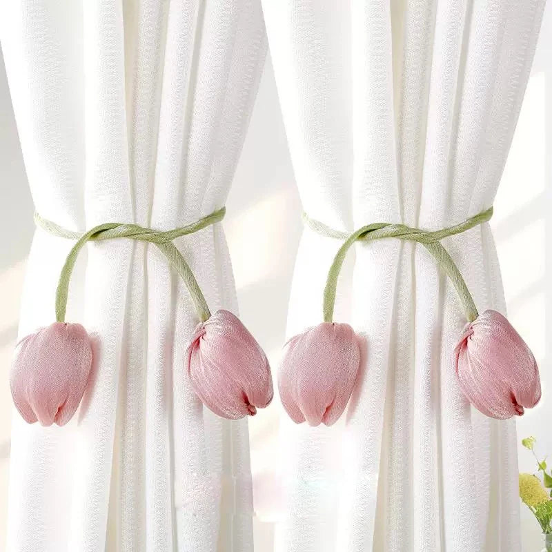 A set of pink tulip-shaped fabric tie backs used to secure white curtains.