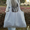 A person is holding a striped tote bag with a brown handle against a blurred outdoor background.