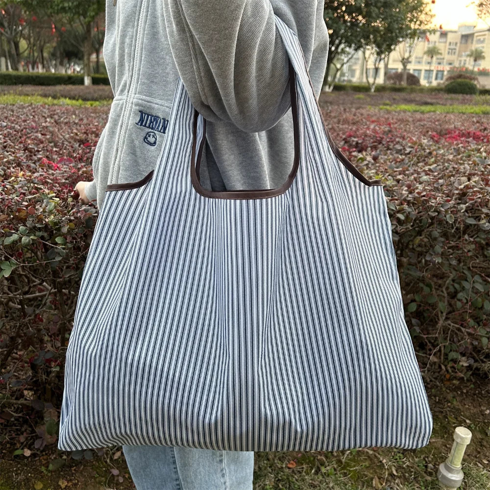 A person is holding a striped tote bag with a brown handle against a blurred outdoor background.