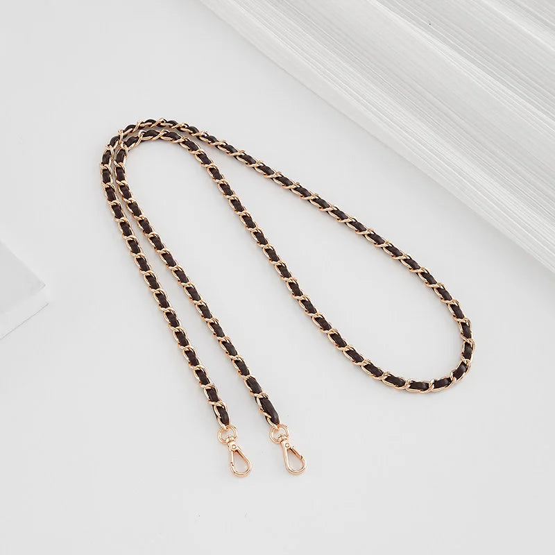 A close-up of a black and gold braided leather shoulder strap with a metal buckle lying on a light surface.