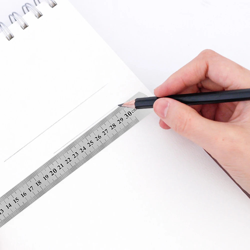 A hand holds a black pencil against a stainless steel precision straight ruler on a white sheet of paper.