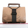 A brown reusable elastic luggage strap with a leather handle and black strap is shown on a reflective surface.