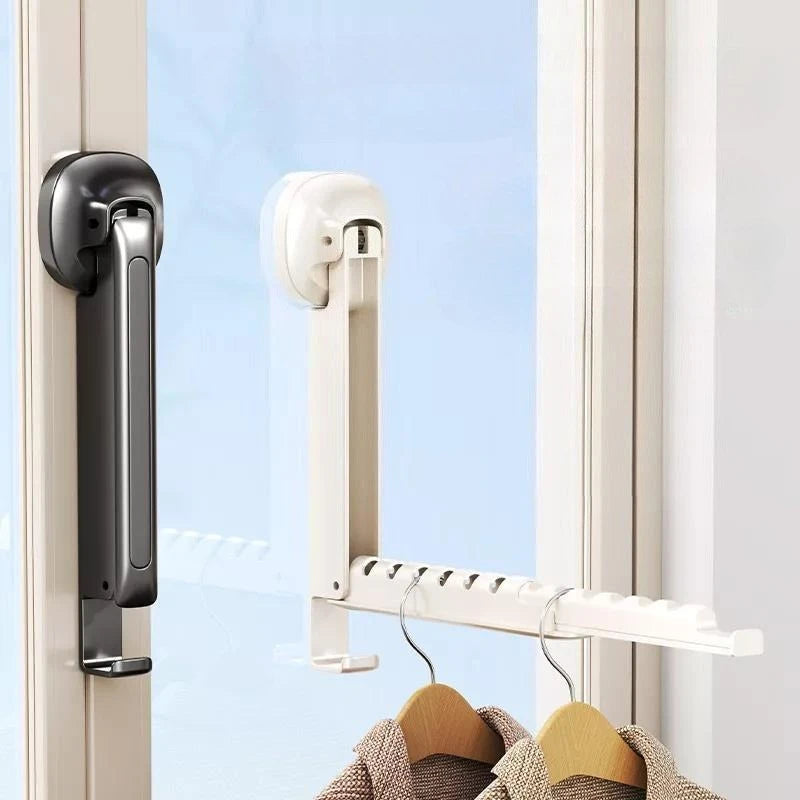A white foldable wall-mounted clothes drying rack with an adhesive mount hanging clothes in a window frame.