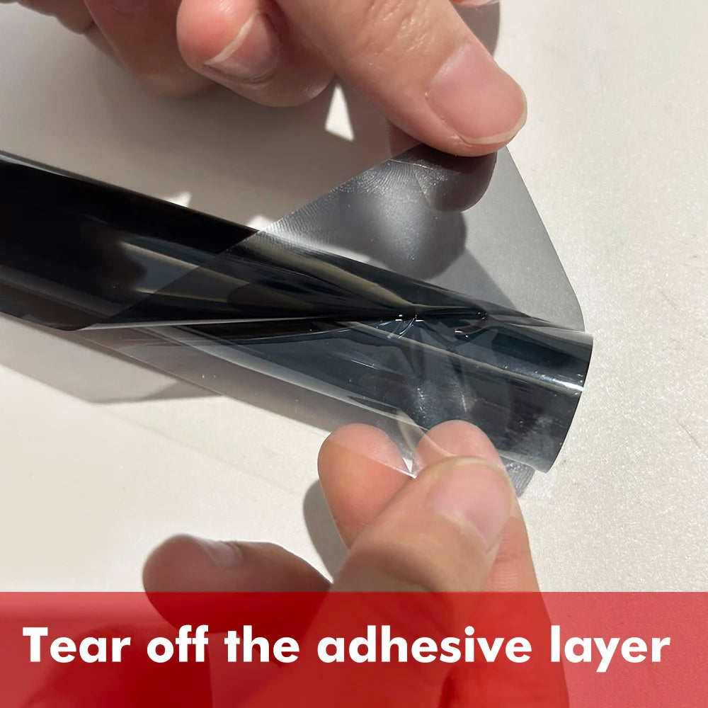 Hands peel off the adhesive layer of a black ceramic car window tint film.