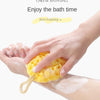 A hand is squeezing a yellow cheese bath ball onto a person's skin during a bath.