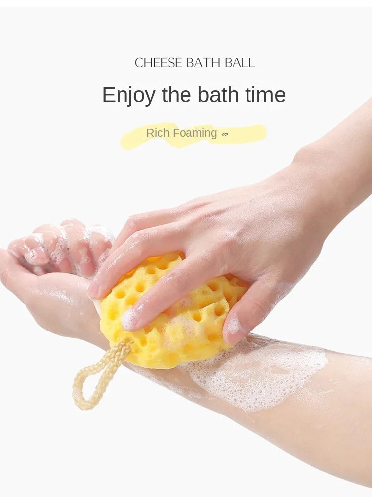 A hand is squeezing a yellow cheese bath ball onto a person's skin during a bath.