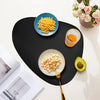 A black placemat features a blue bowl of yellow couscous, a glass of orange liquid, and an avocado slice.