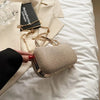 A beige envelope clutch with a gold chain strap resting on white bedding next to a book.
