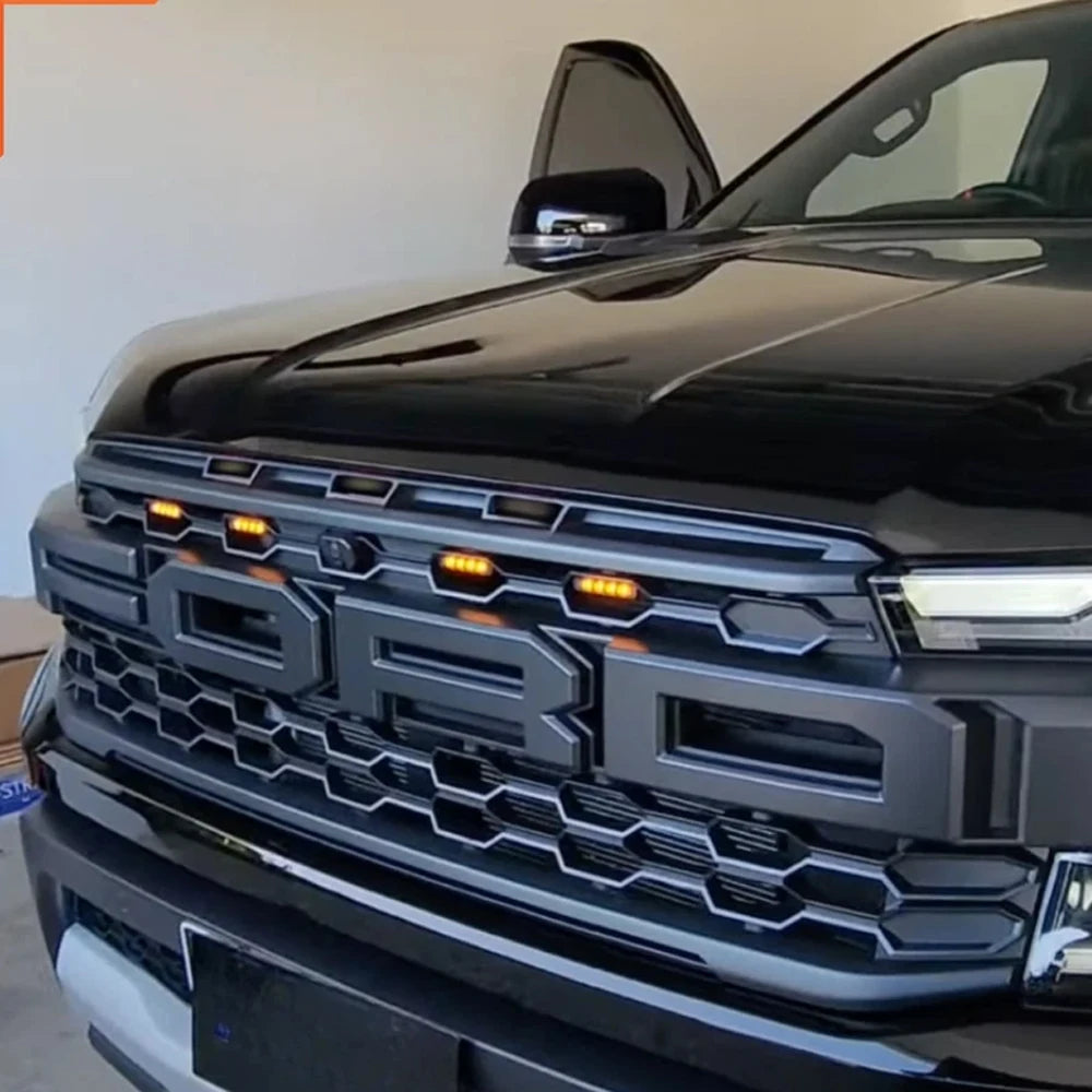 Close-up of the front grille and headlight area of a black Ford Ranger Raptor with amber LED grille lights installed.
