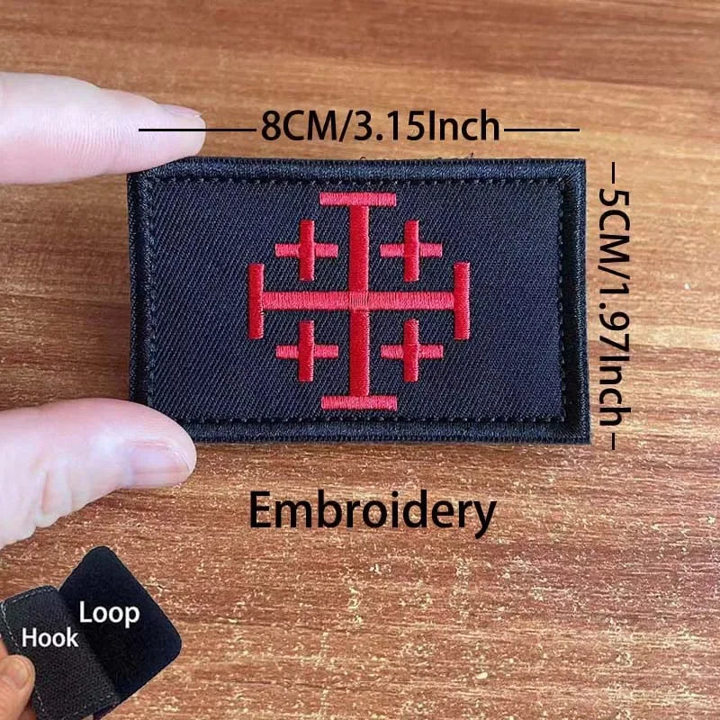 A black embroidered tactical patch featuring a red cross design on a wooden surface.