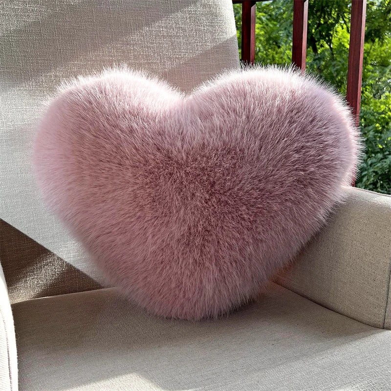 A fluffy pink heart-shaped throw pillow resting on a light-colored outdoor chair.
