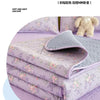 A stack of lavender floral quilted bedspreads and pillows with a fluffy white toy in the background.