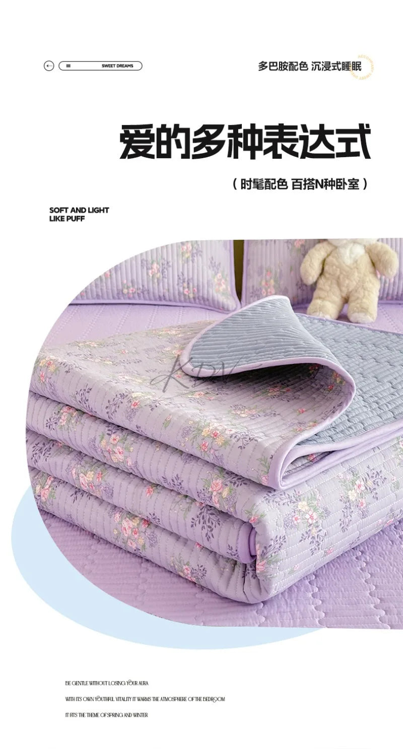 A stack of lavender floral quilted bedspreads and pillows with a fluffy white toy in the background.