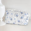 White quilted cosmetic pouch with blue floral print and lace trim resting on a white surface.