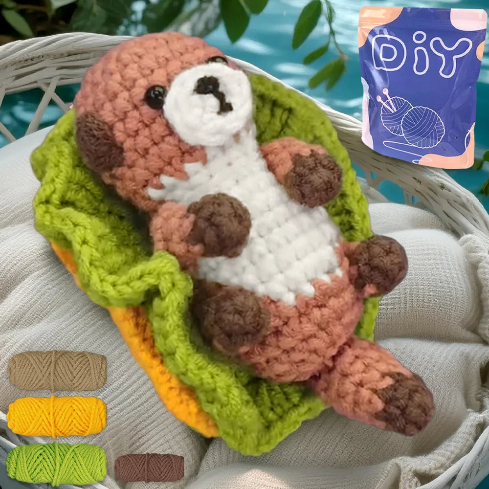 A finished crochet amigurumi of a brown animal nestled in a green fabric, with yarn balls displayed nearby.