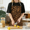 A person wearing a brown and black leopard print kitchen apron is cutting a lemon on a wooden board.