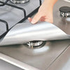 A hand places a silver reusable gas stove burner protector onto a stovetop grate.