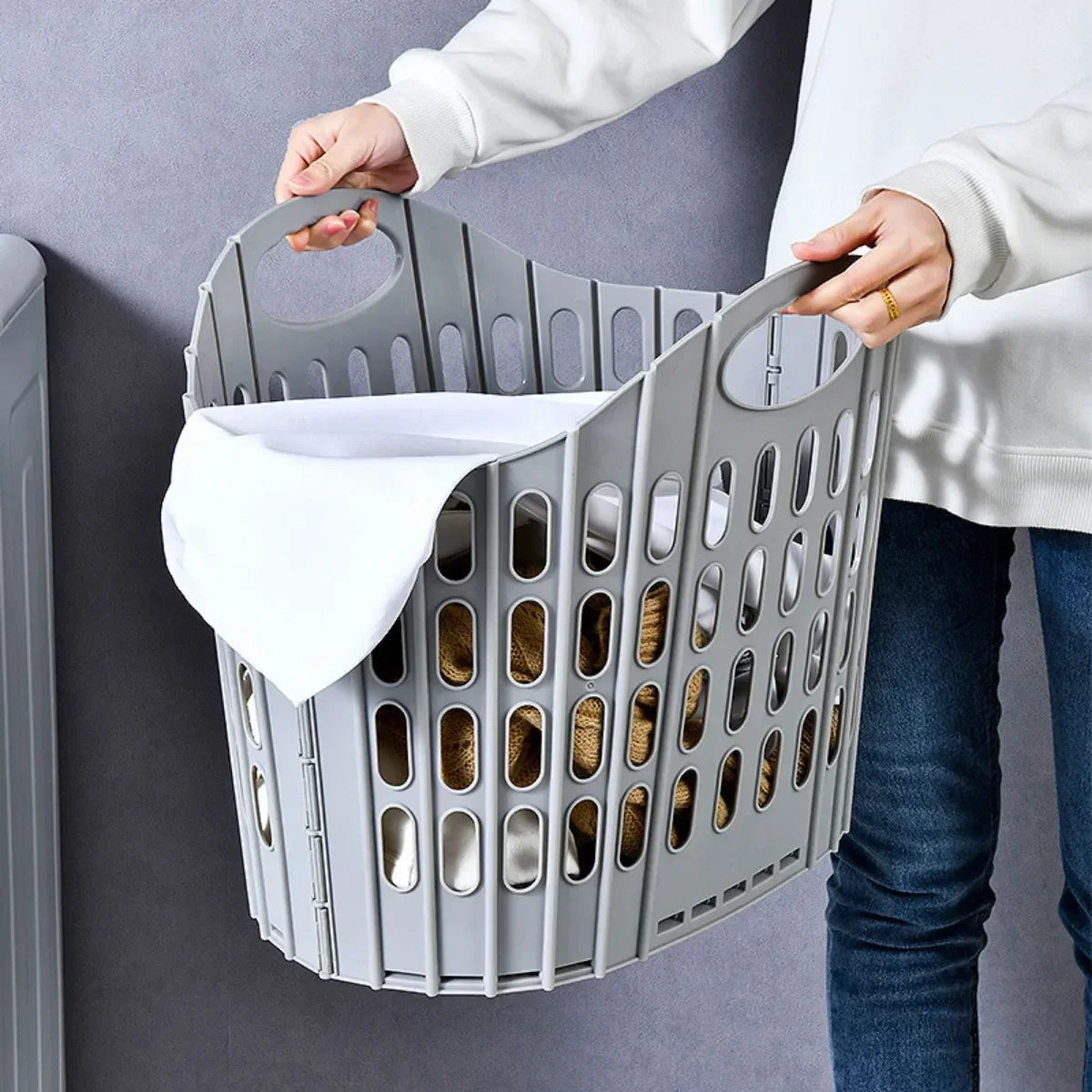 A person is holding a gray modern foldable laundry hamper filled with brown socks and a white cloth.