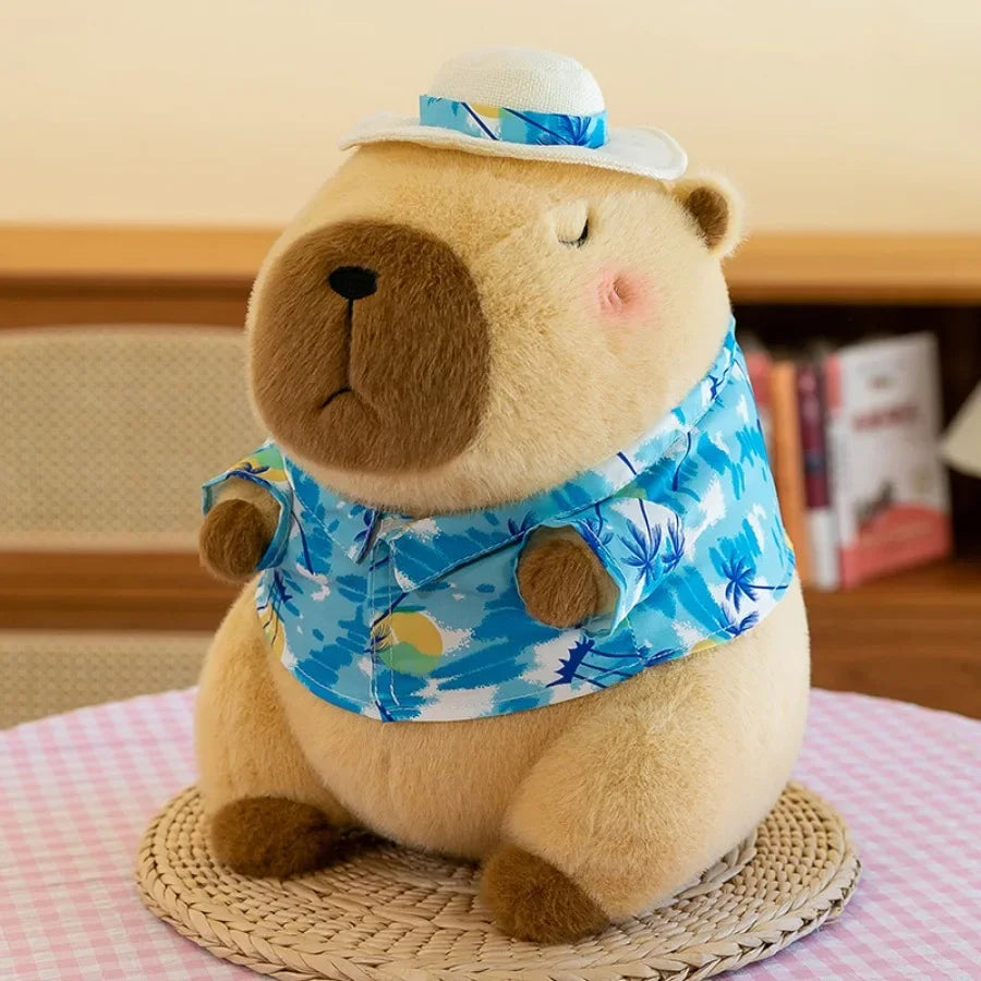 A fluffy beige capybara plush toy wearing a blue patterned shirt and sitting on a woven mat.