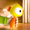 A yellow cartoon animal baby rattle with an orange hand grasping it, shown in a close-up shot.