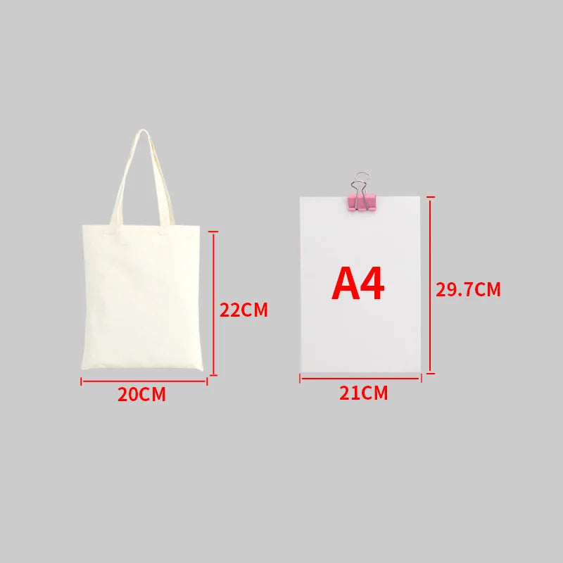 A white canvas shopping tote bag with a foldable design shown next to an A4 sized paper.