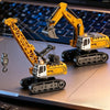 A yellow 1:64 scale remote control construction vehicle with an excavator arm and lights on a desk.