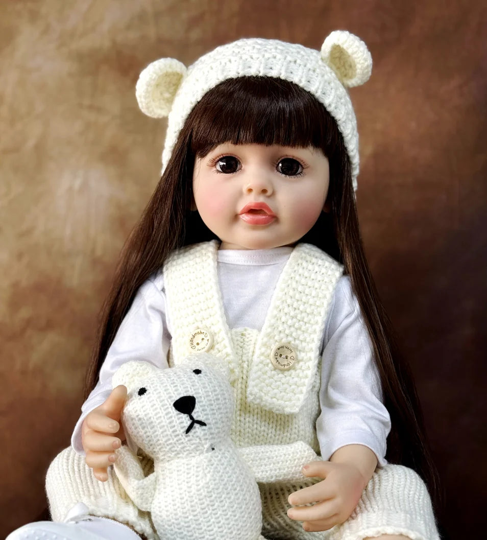 A lifelike silicone baby doll with long dark hair wearing a white knitted headband and vest.