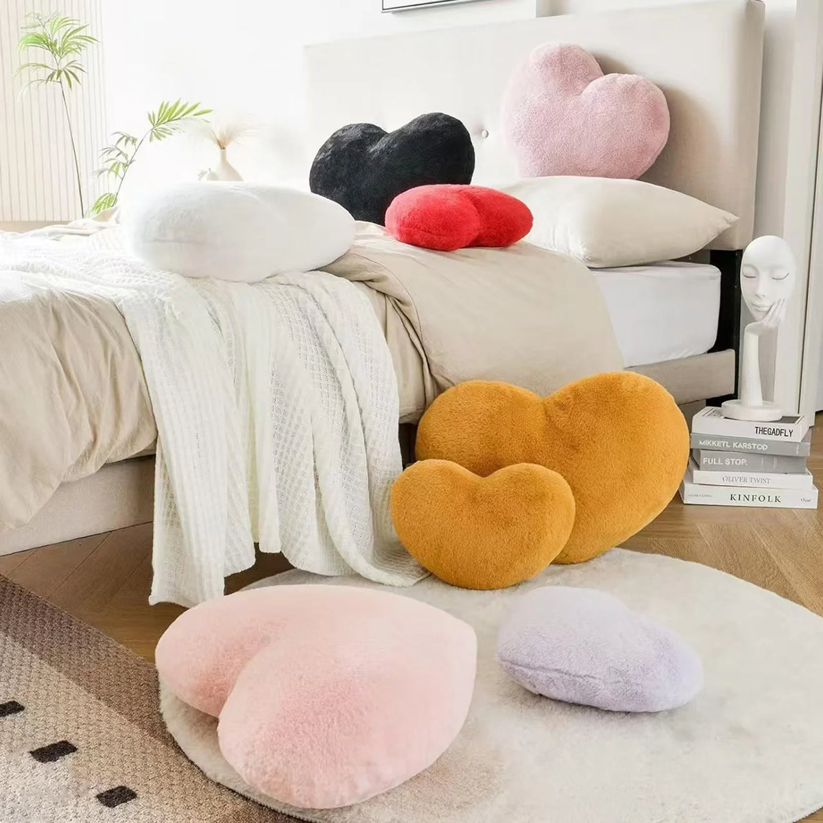 A collection of heart-shaped plush throw pillows in pink, yellow, and black resting on a beige blanket and white bedding.