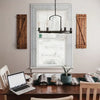 A close-up of a wooden table with a laptop, cups, and decorative items in front of a window with white blinds.