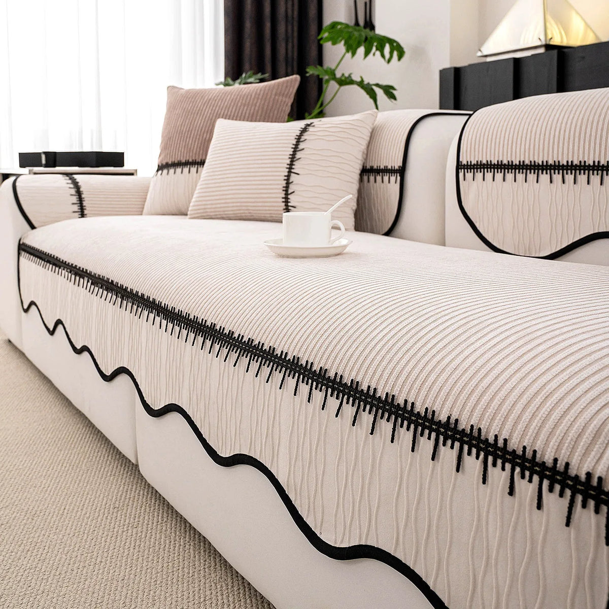 A beige striped chenille sofa cover with a black pleated hem displayed on a white sofa.