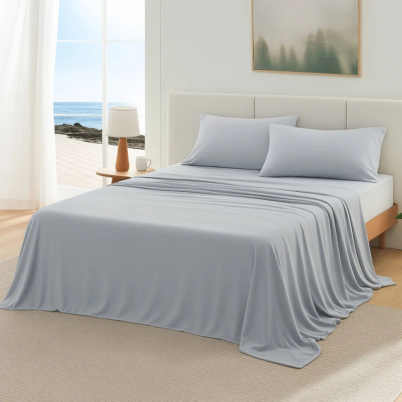 A light blue ice silk blanket is draped over a bed with white pillows and a neutral-toned duvet on a light wood floor.