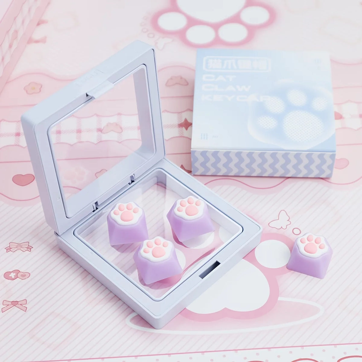 A clear plastic case holds purple silicone cat paw keycaps and a box labeled Cat Claw Keycap for MX Switches on a pink backgr