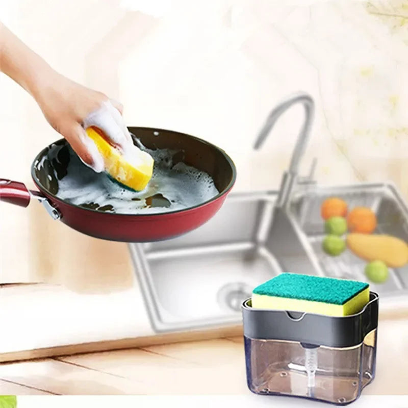 A hand is using a press-type portable soap dispenser to wash a yellow lemon in a kitchen sink.
