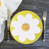 A yellow plate with a white daisy design is set on a dark wooden surface next to a fork and knife.