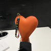 An orange heart-shaped PU coin purse with a black wrist strap is held up against a dark background.