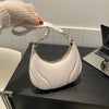 A white textured crossbody bag with gold hardware is held by a hand on a dark surface.
