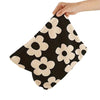 A black and beige floral corduroy makeup bag with a secure zipper being held by a hand.