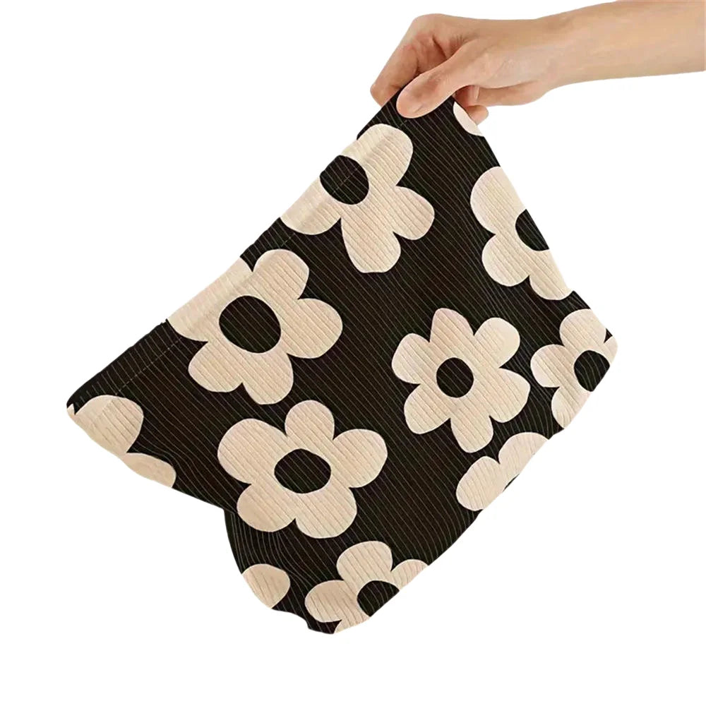 A black and beige floral corduroy makeup bag with a secure zipper being held by a hand.