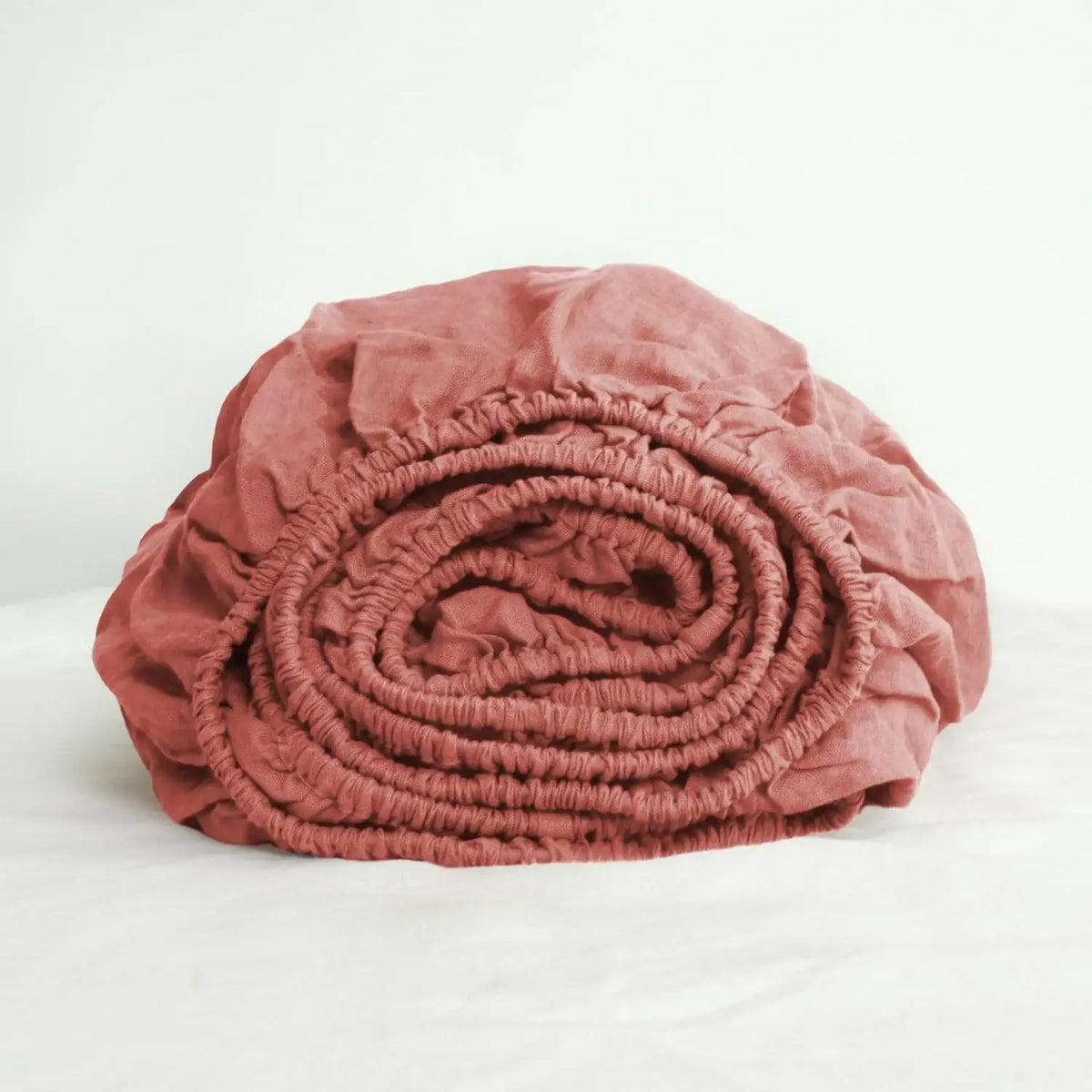A rolled terracotta pink linen fitted sheet with deep pockets.