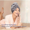 A woman is smiling while using a gray knitted hair towel wrap to dry her hair.