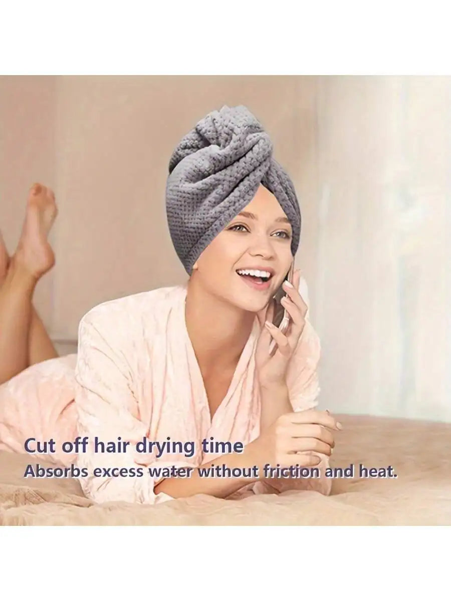 A woman is smiling while using a gray knitted hair towel wrap to dry her hair.