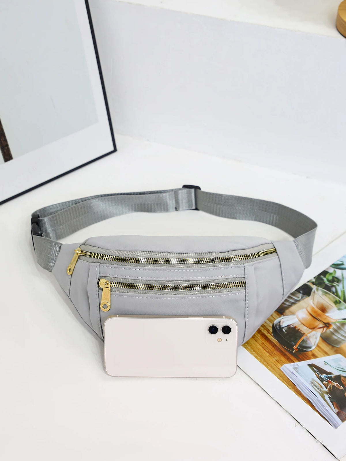 A light gray nylon waist pack with a zippered pocket and a smartphone attached, resting on a white surface.