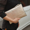 A person holds a beige crocodile-embossed PU leather envelope clutch against a white car door.