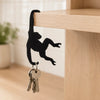 A black monkey-shaped wooden wall hook with a key attached, hanging over a light wood shelf.
