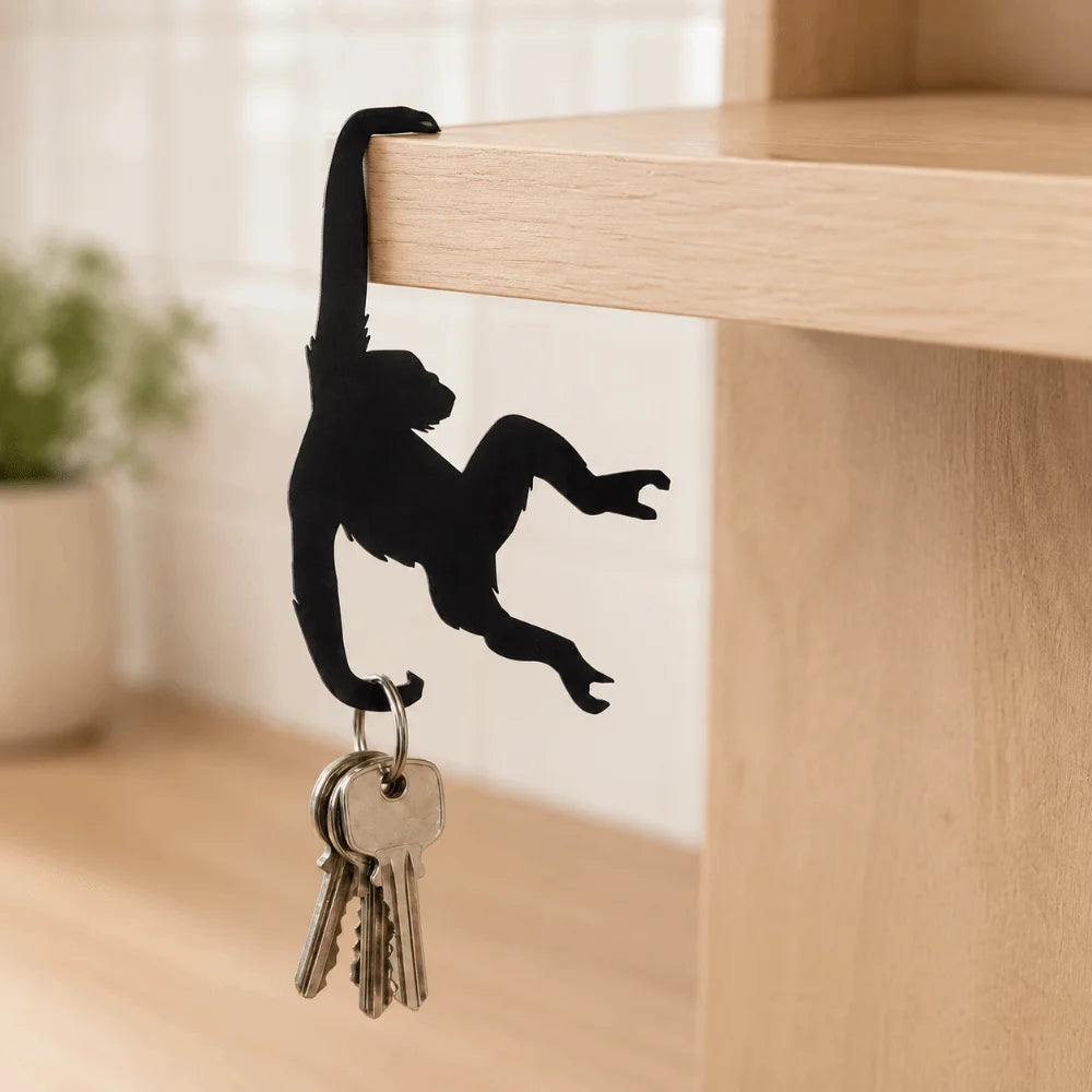 A black monkey-shaped wooden wall hook with a key attached, hanging over a light wood shelf.
