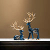 A set of two blue resin deer figurines with golden antlers displayed on a wooden surface.