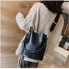 A woman wearing a beige sweater holds a black alligator pattern crossbody bag.